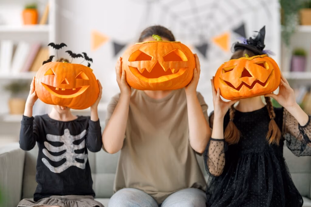 A mother and two children holding up carved pumpkins to their faces.