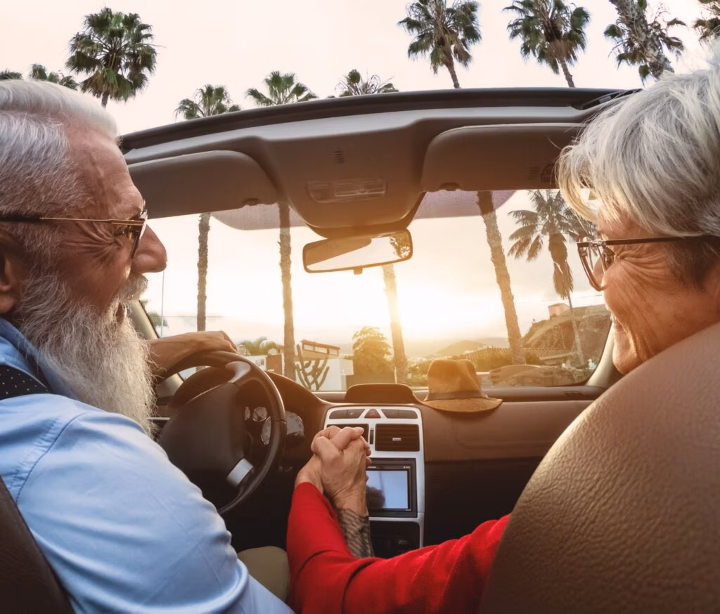 A happy older couple driving in a convertible car.