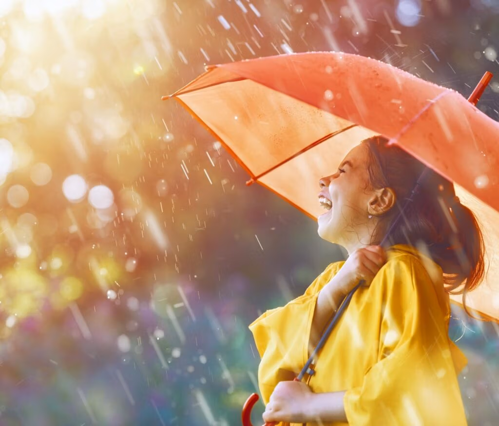 A girl laughing in the rain under an umbrella.