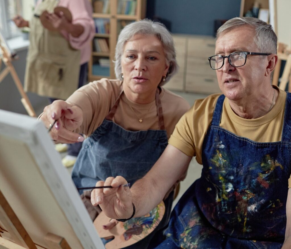 An older couple painting at an easel together.